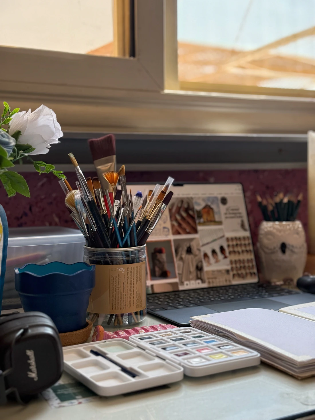 Brushes, a watercolour palette and sketchbooks on a sunlit studio desk