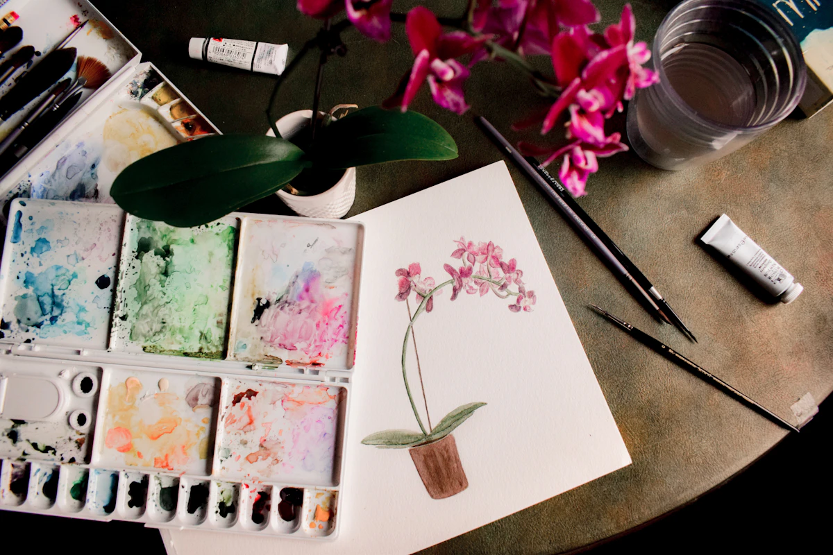 Watercolour palette with brushes and a freshly painted flower illustration